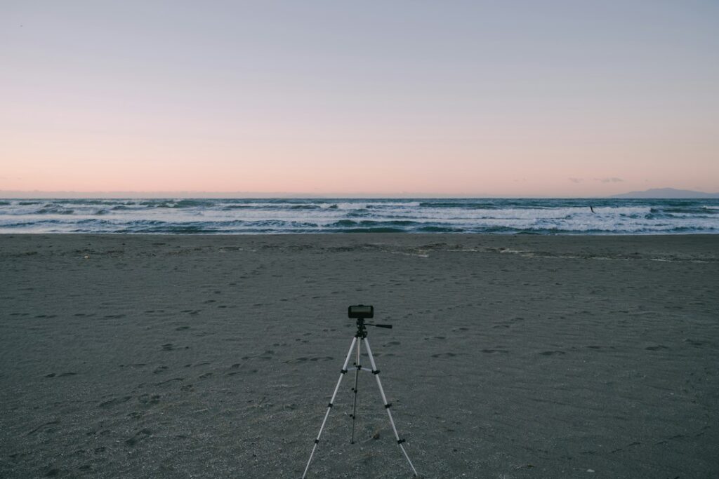 A compact travel tripod set up on a beach facing the ocean
