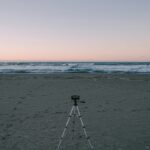 A compact travel tripod set up on a beach facing the ocean