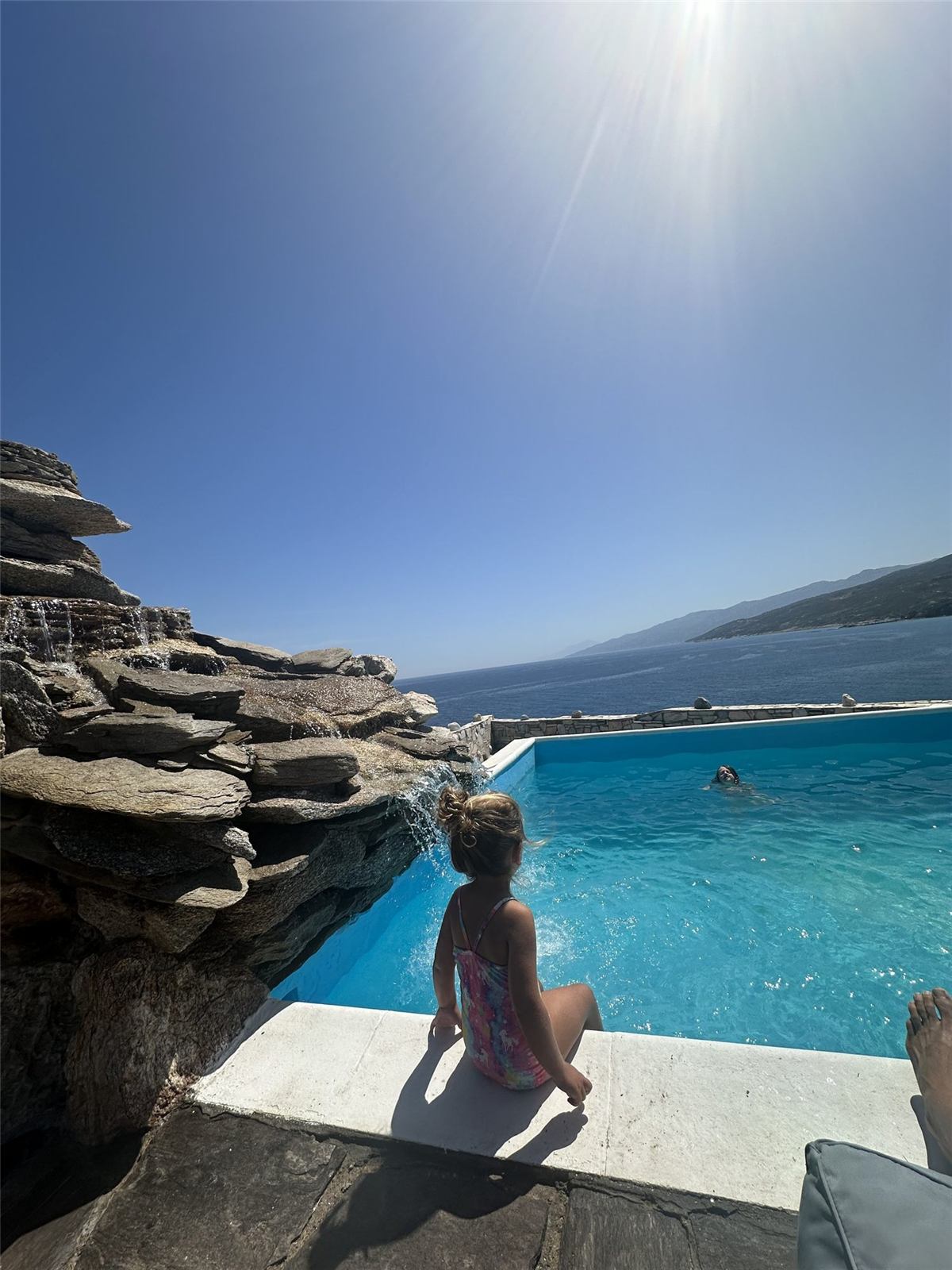 One of the Fredette girls sitting at the edge of a pool overlooking the Aegean Sea on the Greek island of Syros