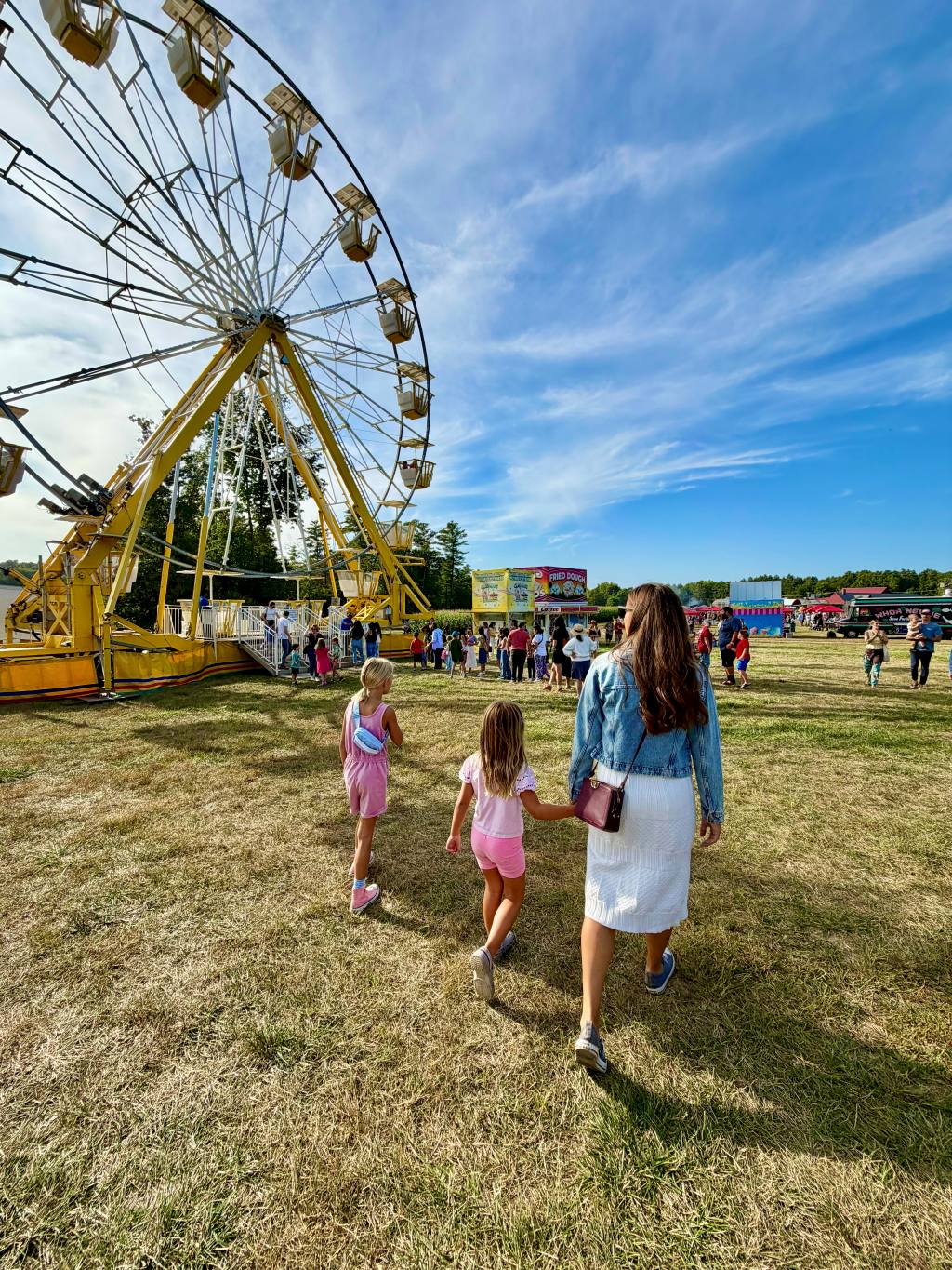 Kailah walking hand in hand with the two girls toward a Ferris wheel at a New Hampshire fall fair