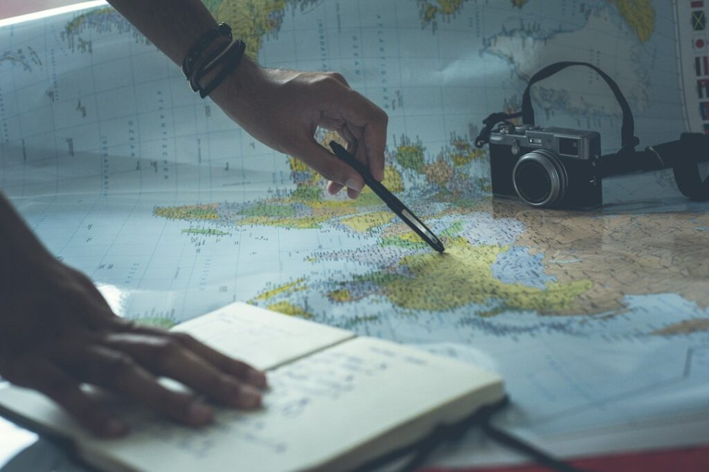 Traveler writing notes beside a laptop while planning a monthly budget