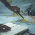 Traveler writing notes beside a laptop while planning a monthly budget